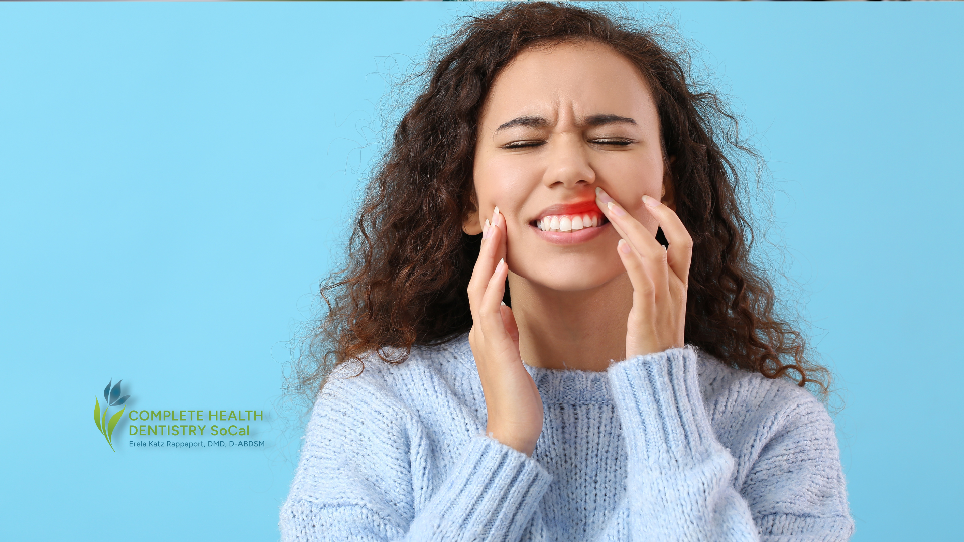 A woman in a blue sweater is holding her face in pain.