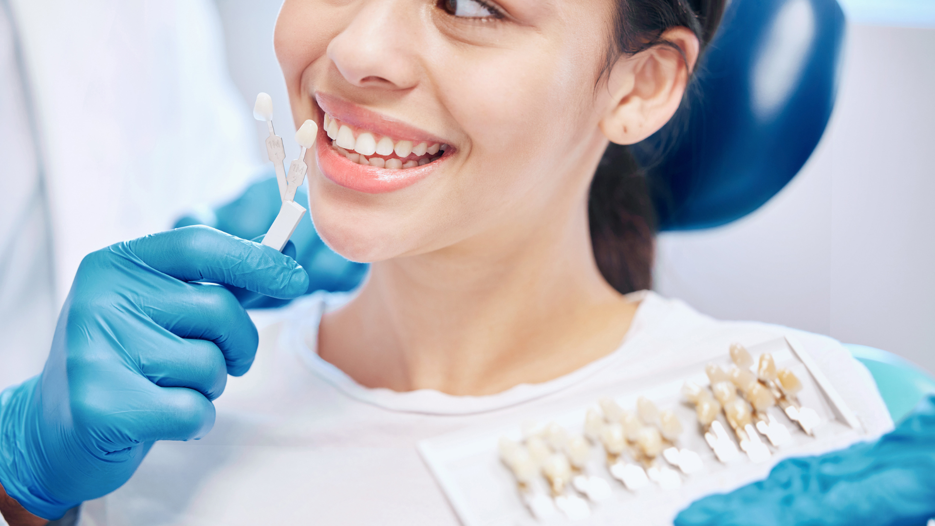 Dentist comparing teeth shade with a color guide on a smiling patient's teeth in a dental office.