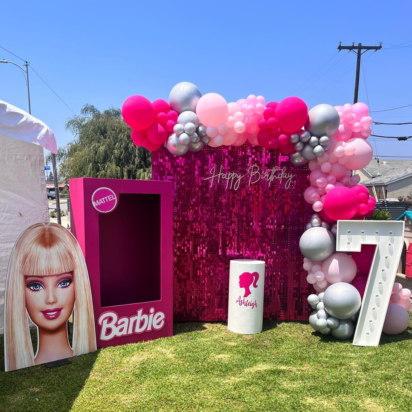 a barbie box is sitting in the grass next to a balloon arch