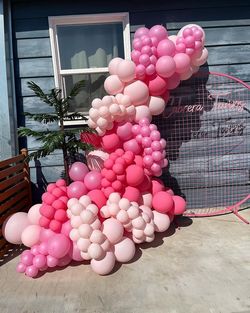 a bunch of pink balloons are sitting in front of a house