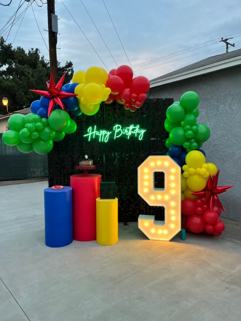 a neon sign that says happy birthday is surrounded by balloons