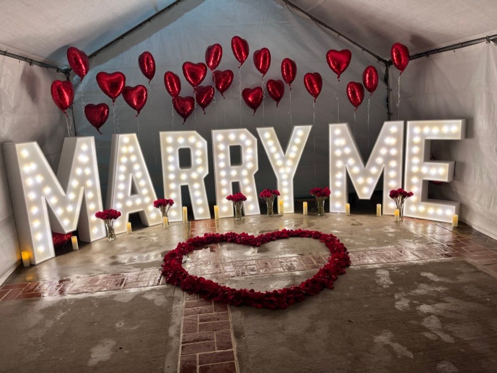 a sign that says marry me with balloons and roses
