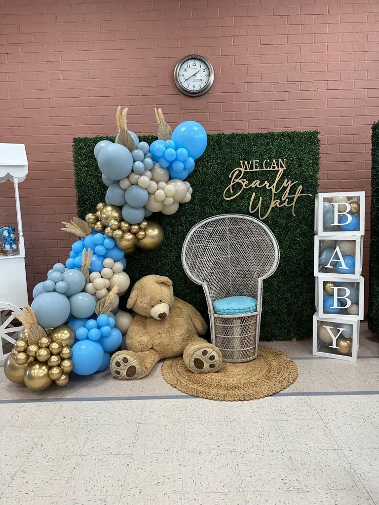 a teddy bear is sitting in a chair in front of a wall of balloons