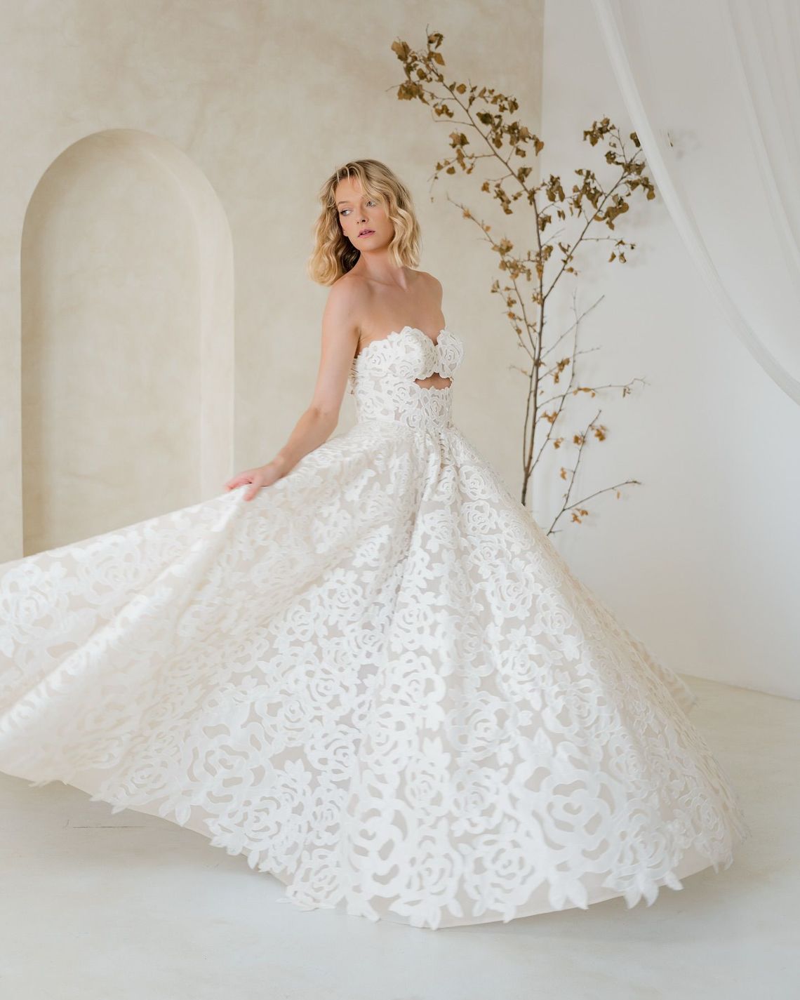 A woman in a white wedding dress is standing in front of a white wall.