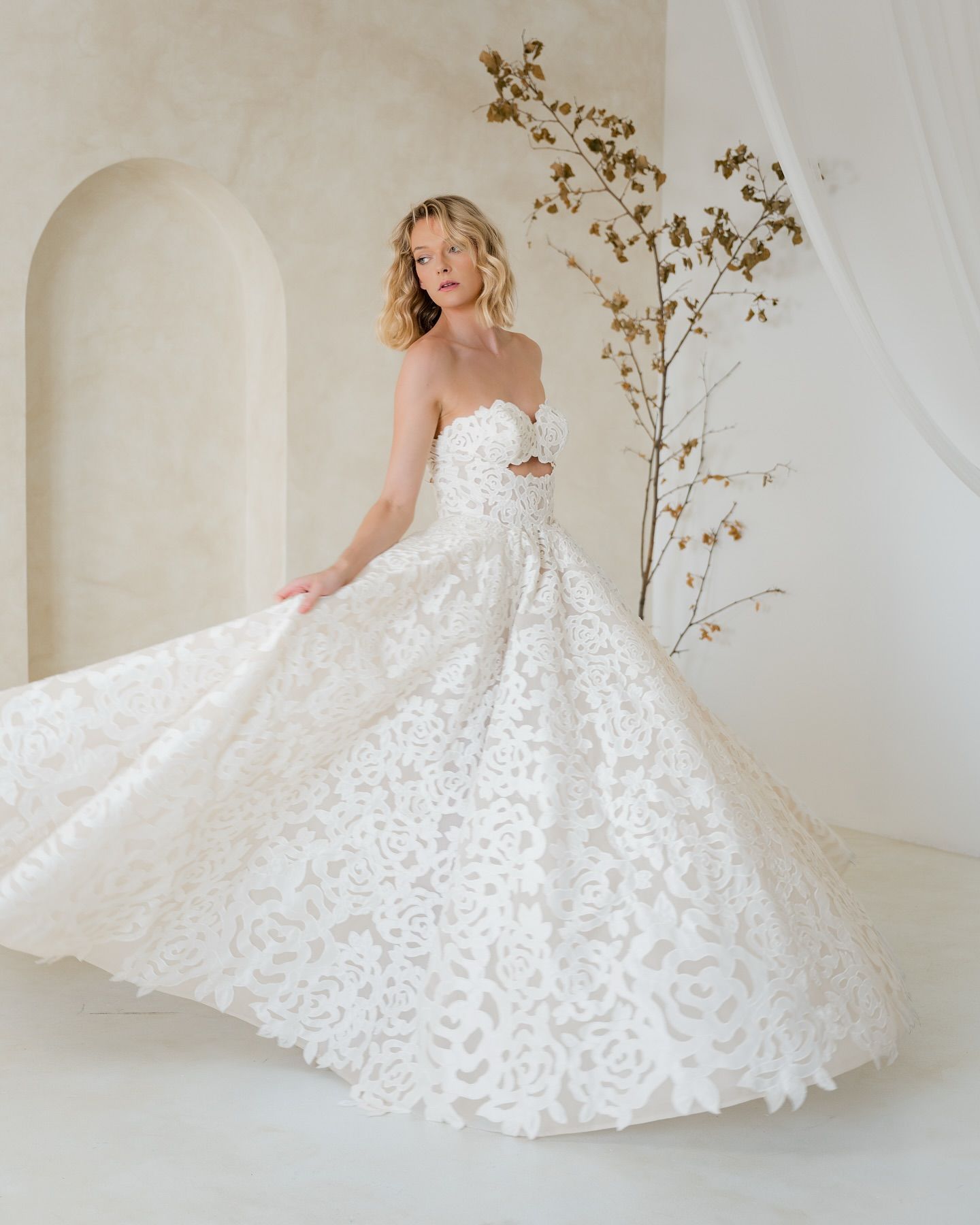A woman in a white wedding dress is standing in front of a white wall.