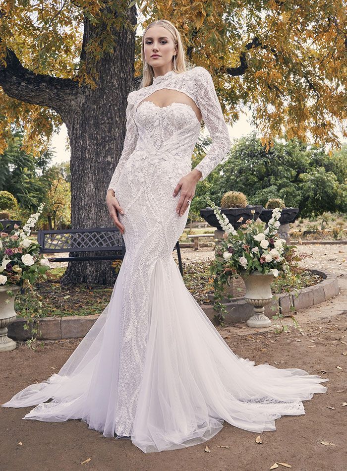 A woman in a white wedding dress is standing in front of a tree.
