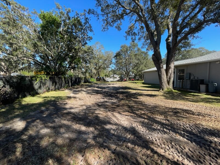 Yellow excavator on a dirt ground, near piles of rocks, trees in the background.