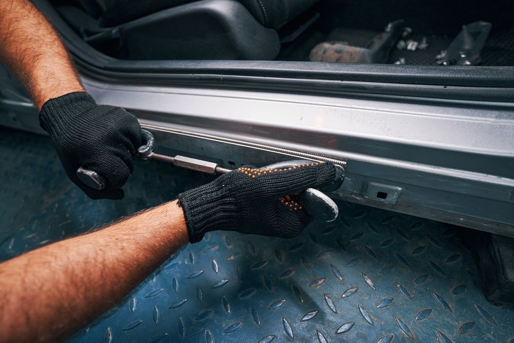 Gloved hands measuring a car door panel with a tape measure in a workshop