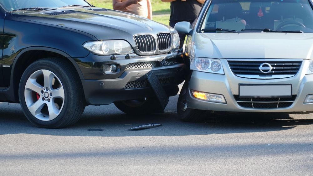 Two cars collided front-to-front on a road, with a black SUV and a silver sedan showing front-end damage.