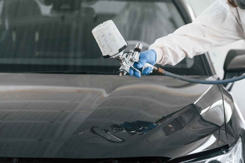 Person spray-painting a black car hood with a spray gun in a workshop