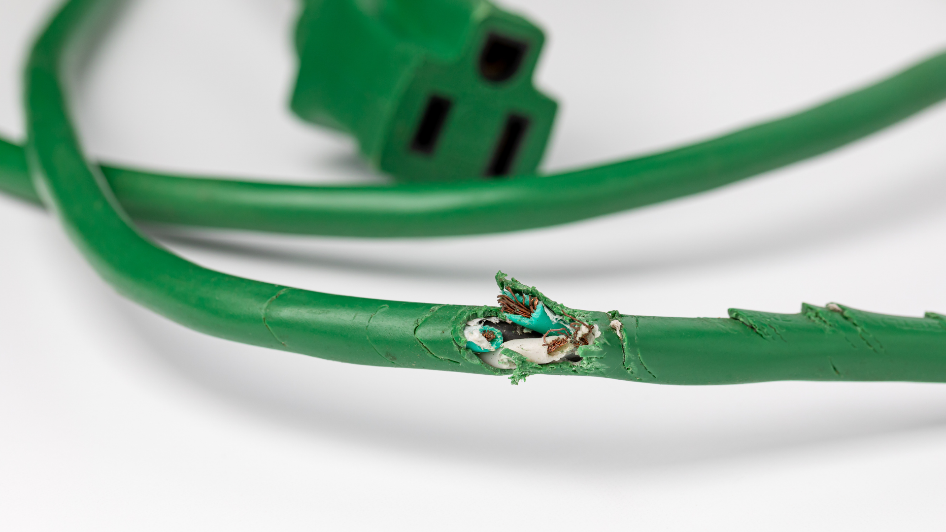 Green electrical cord with a damaged area revealing wires.