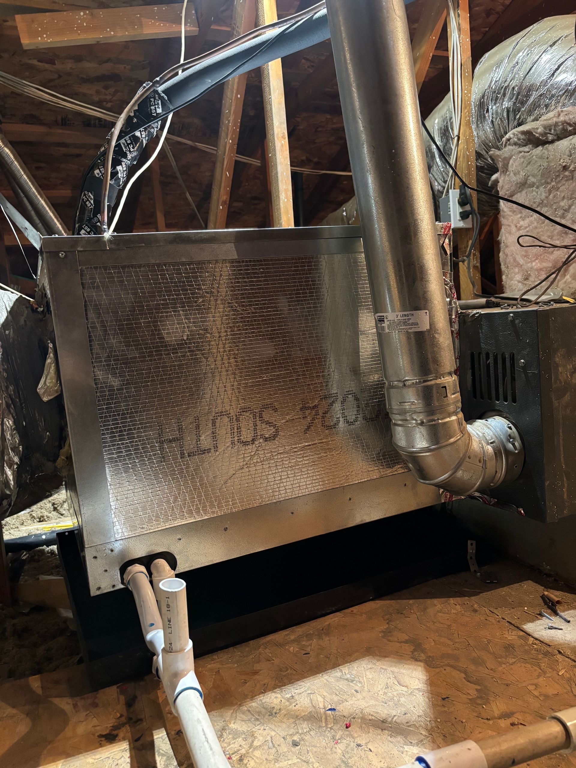 Metal air handler unit in attic with ductwork and PVC pipes.  The unit is silver and connected to a furnace.