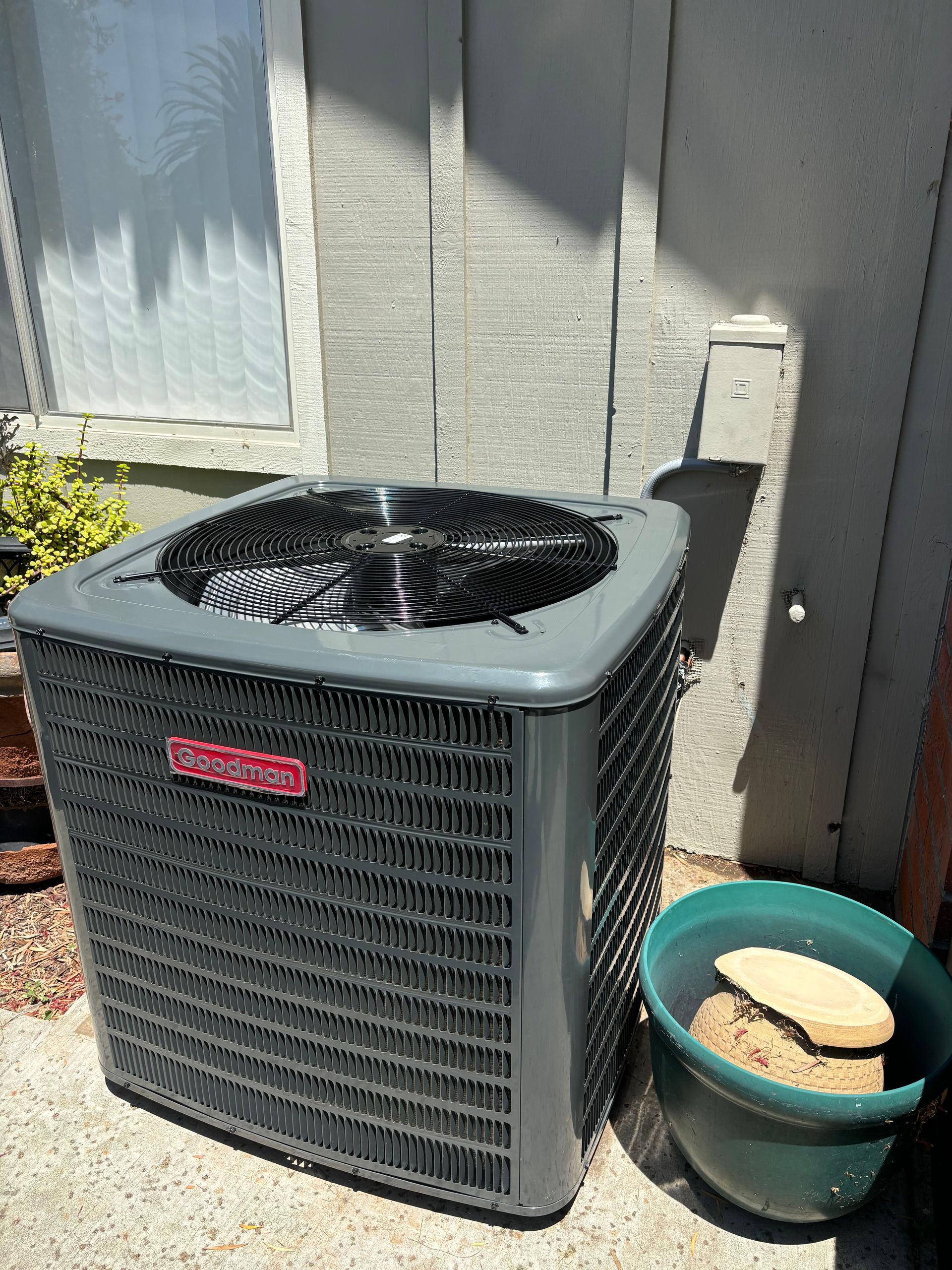 A gray air conditioner is sitting on the side of a building next to a green bowl.