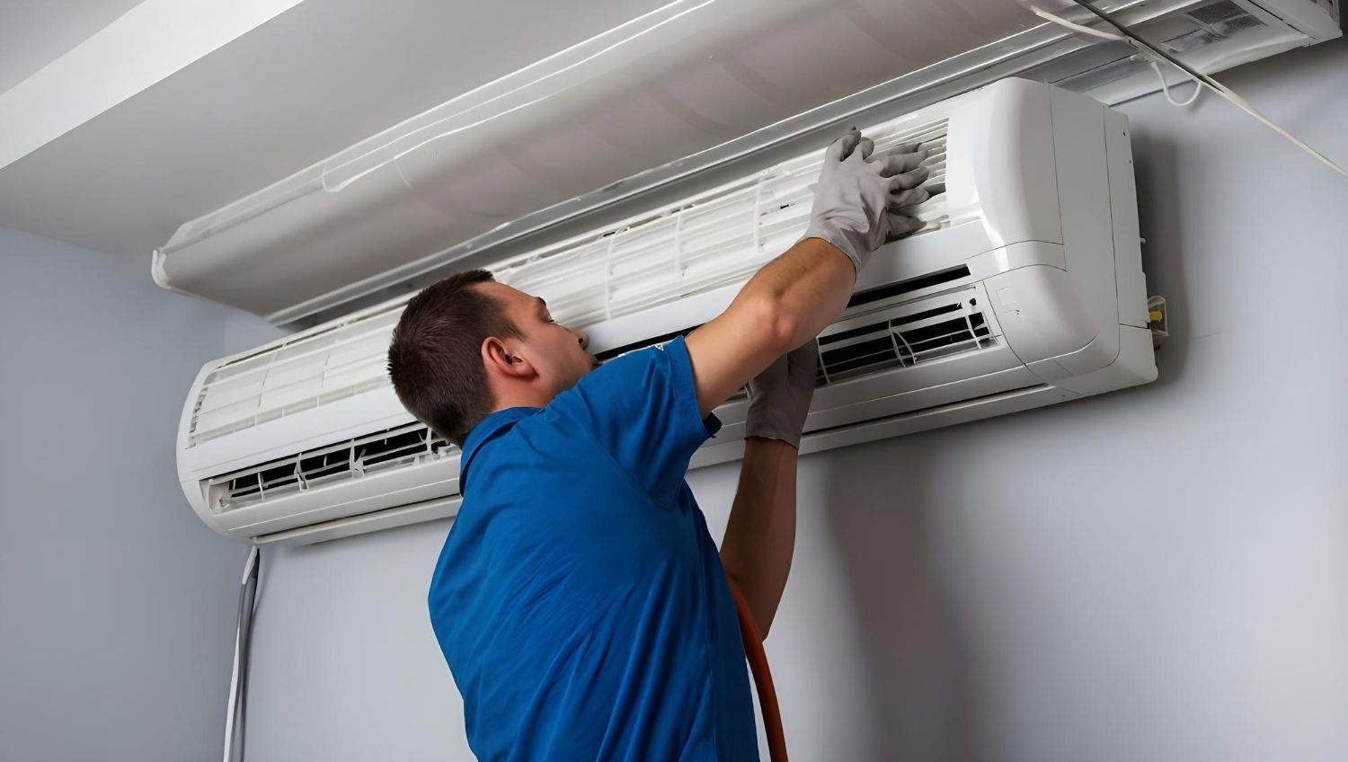 Man in blue shirt, wearing gloves, cleaning a wall-mounted air conditioner.