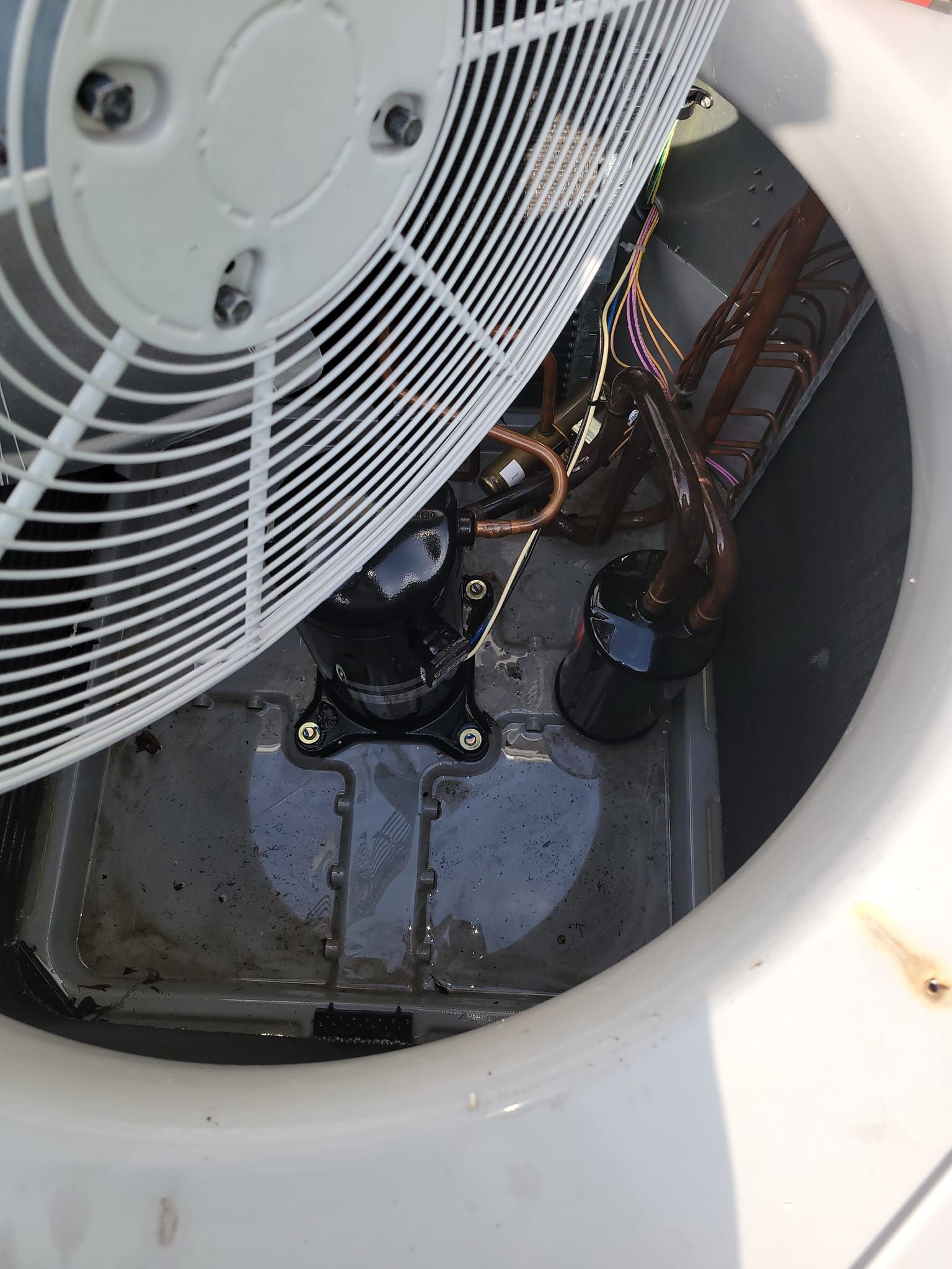 Top-down view of an outdoor air conditioning unit. Fan, compressor, and copper tubing visible inside a gray metal casing.