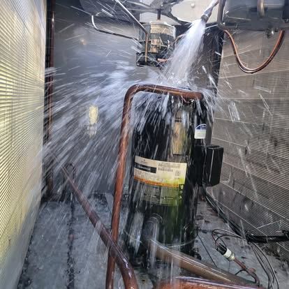 Water spraying on a large, black compressor in a mechanical room, copper tubing visible.