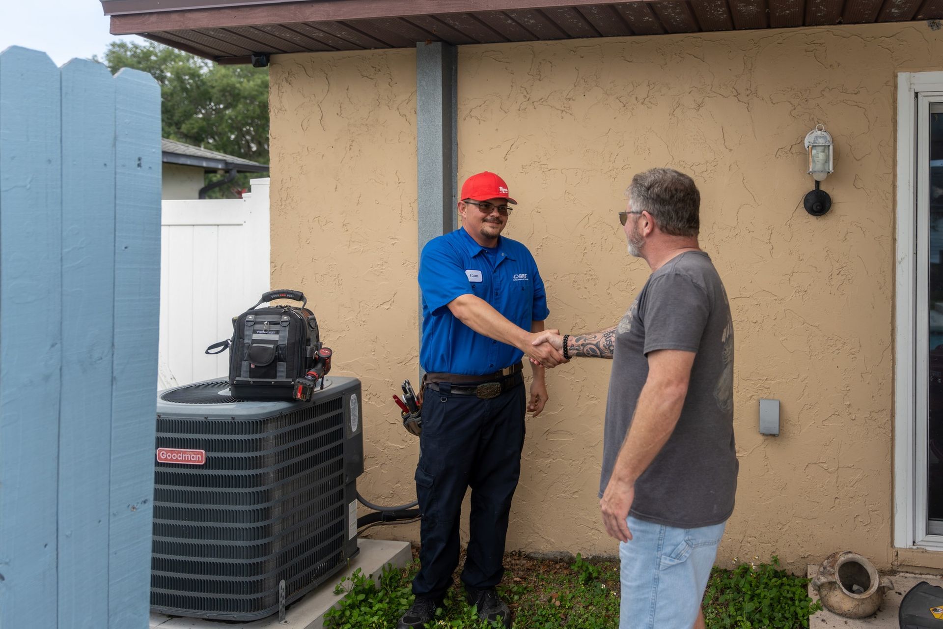 HVAC technician and customer shaking hands near an air conditioning unit and house.