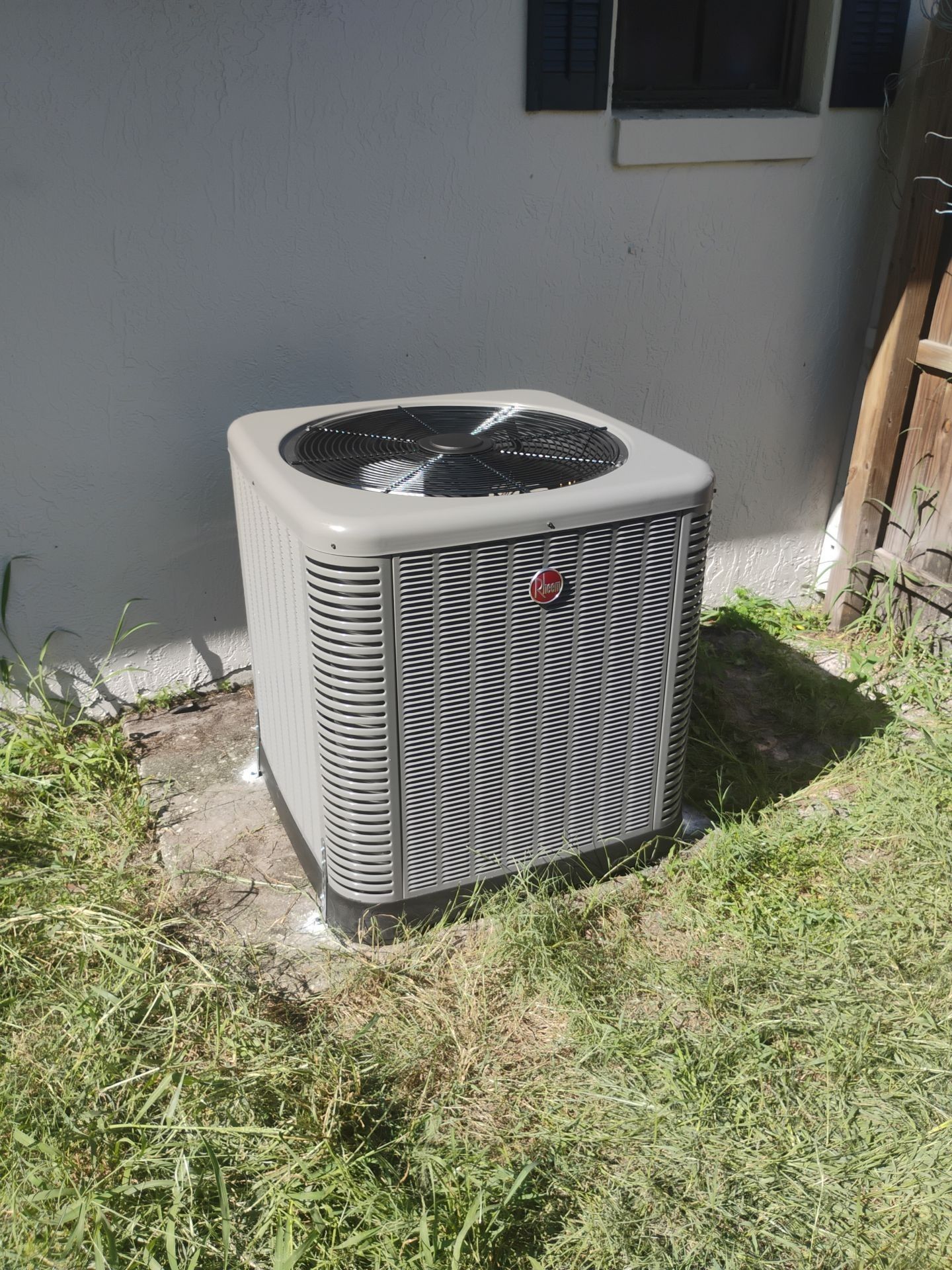 Air conditioner unit outside a building, near a window. Yellow building with green grass.