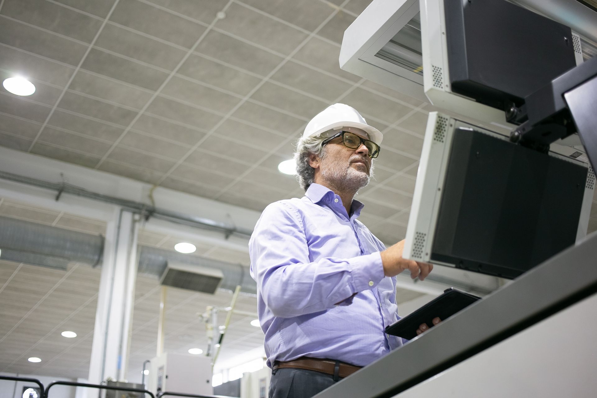 A man wearing a hard hat and goggles is working on a computer in a factory.