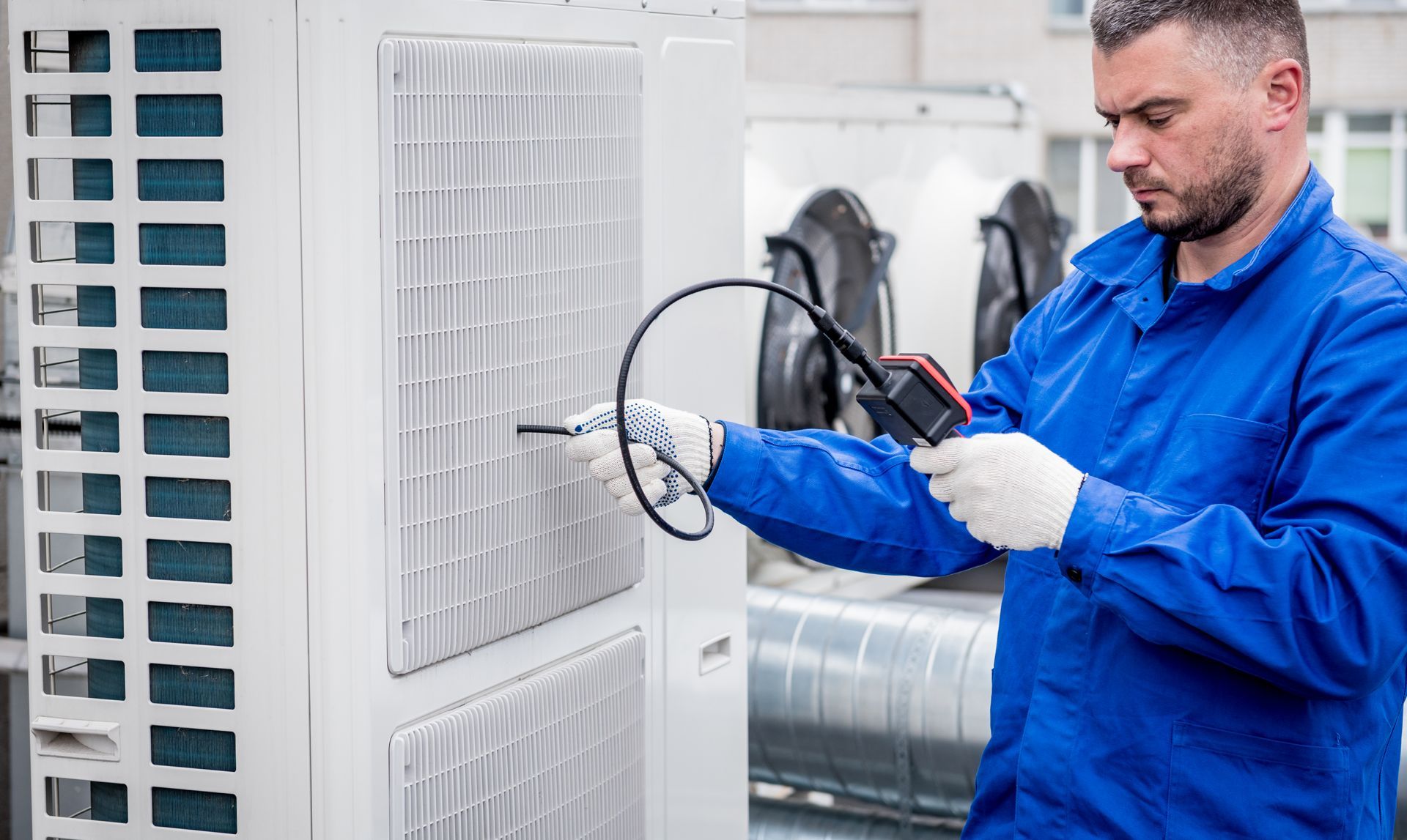 A man in a blue uniform is working on an air conditioner.
