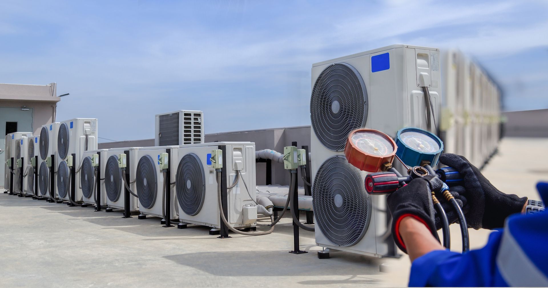 A man is holding a gauge in front of a row of air conditioners.
