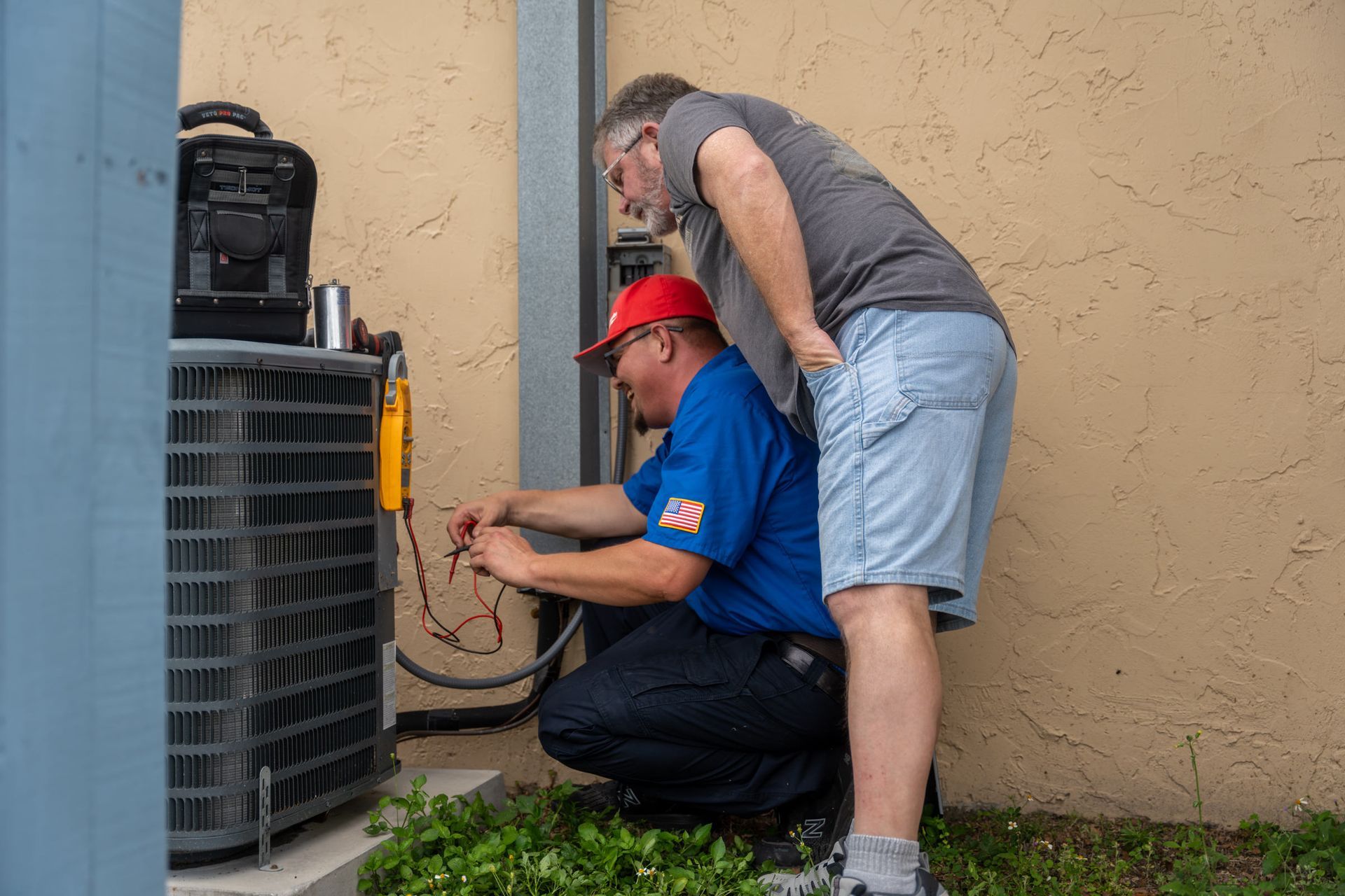 Two men are working on an air conditioner outside of a building.
