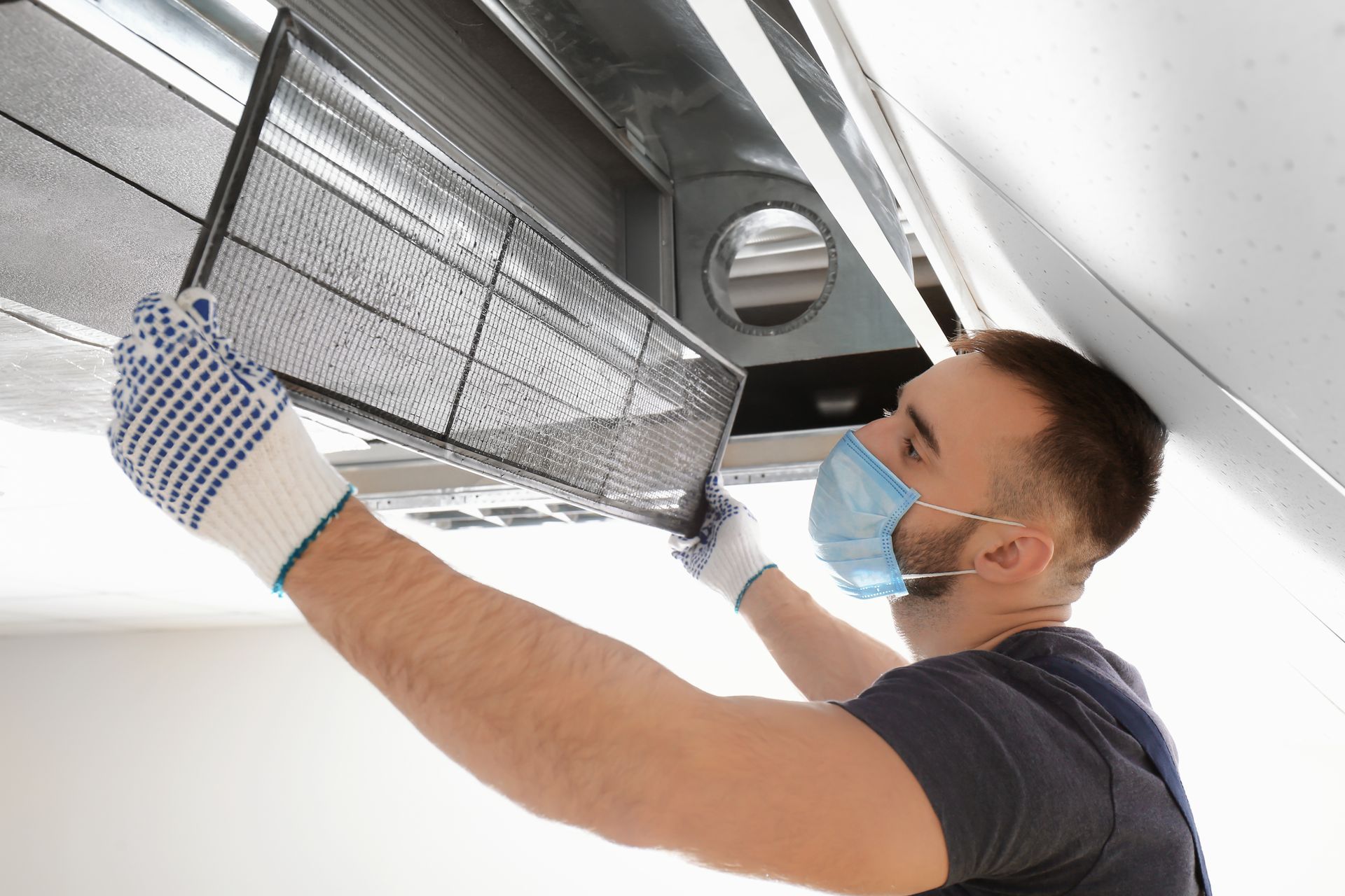 A man wearing a mask and gloves is cleaning an air conditioner.