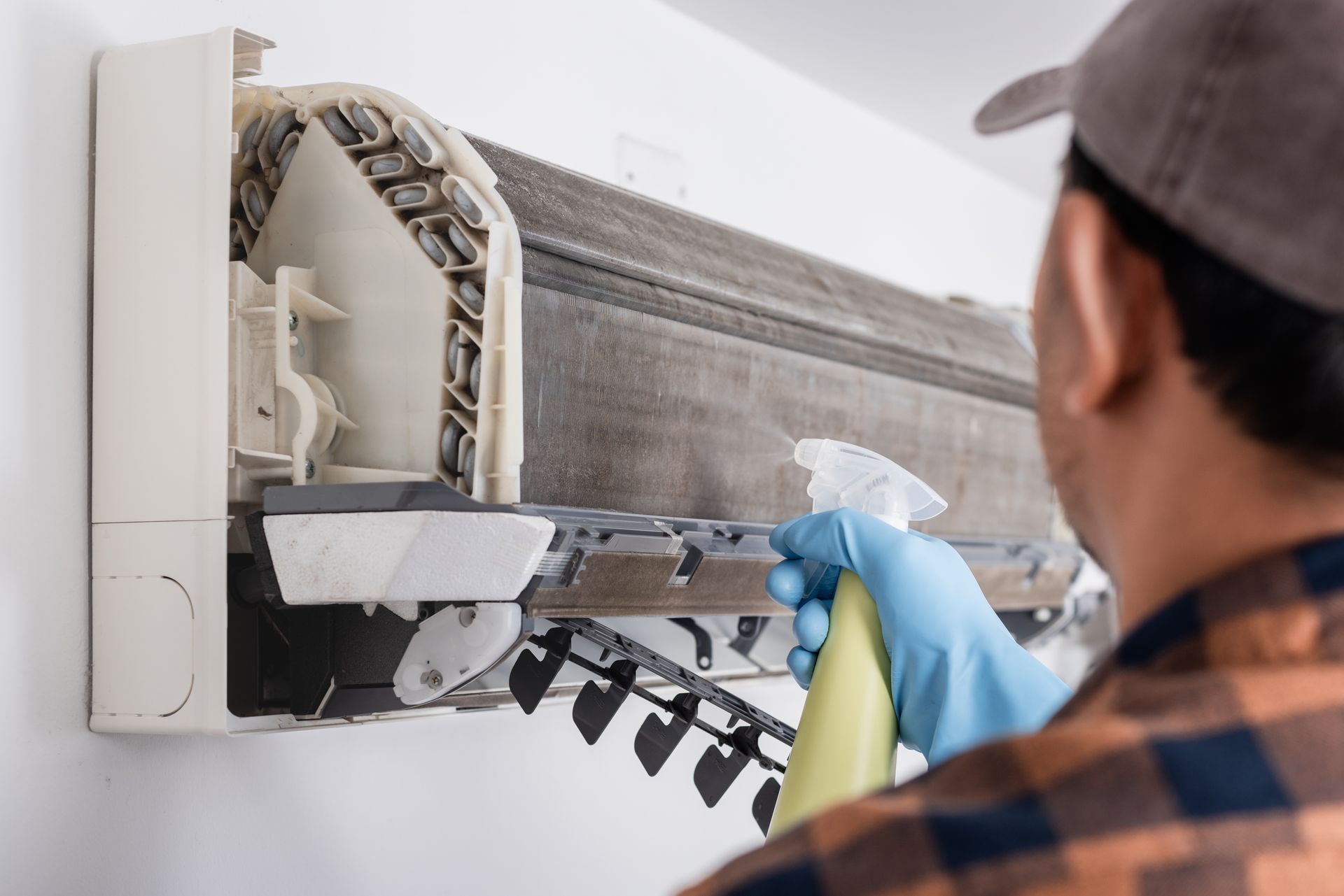 A man is cleaning an air conditioner with a spray bottle.