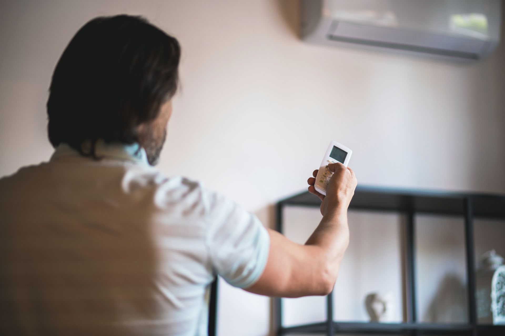 A man is holding a remote control in front of an air conditioner.