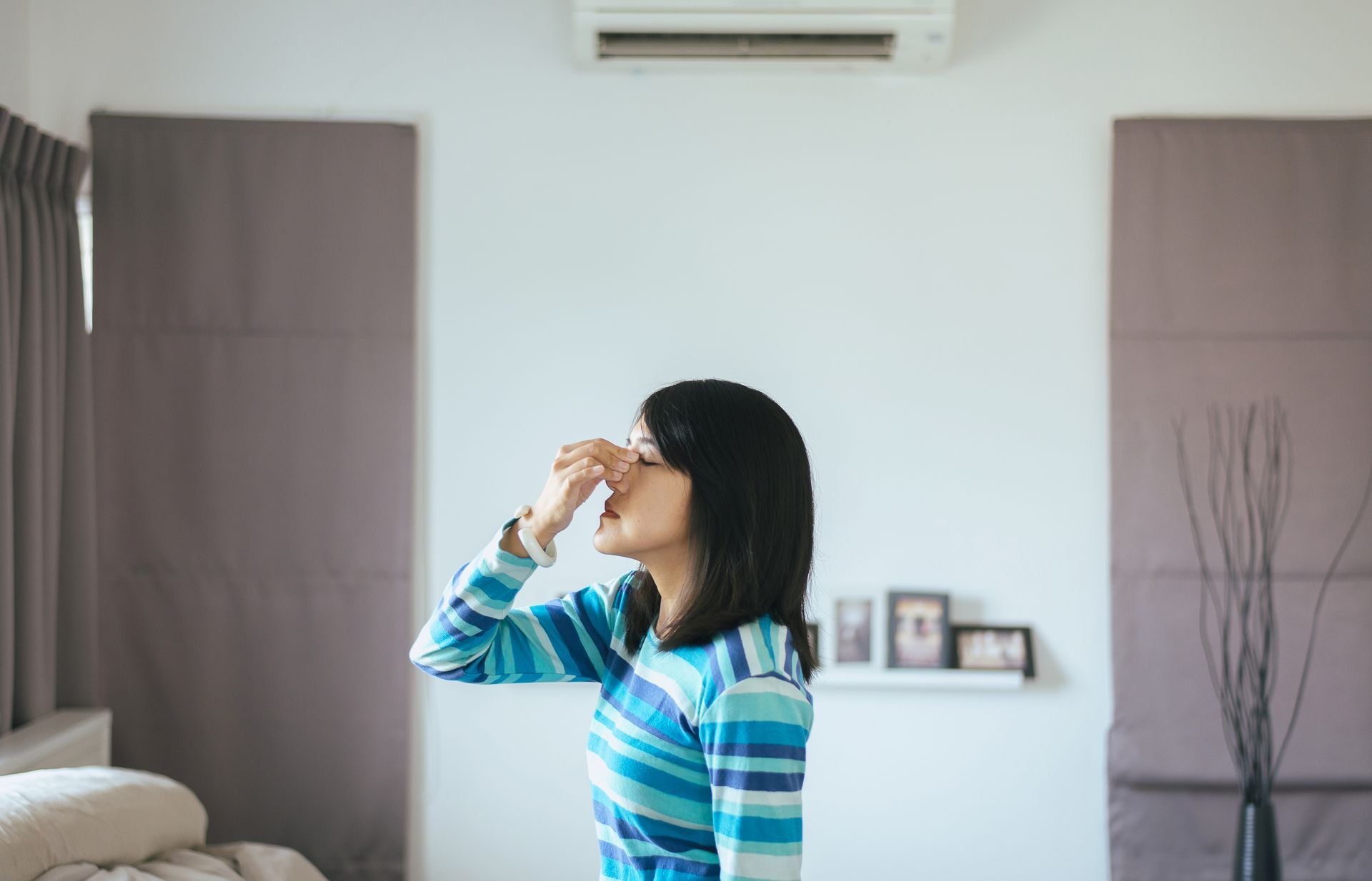 A woman is covering her nose while standing in a living room.