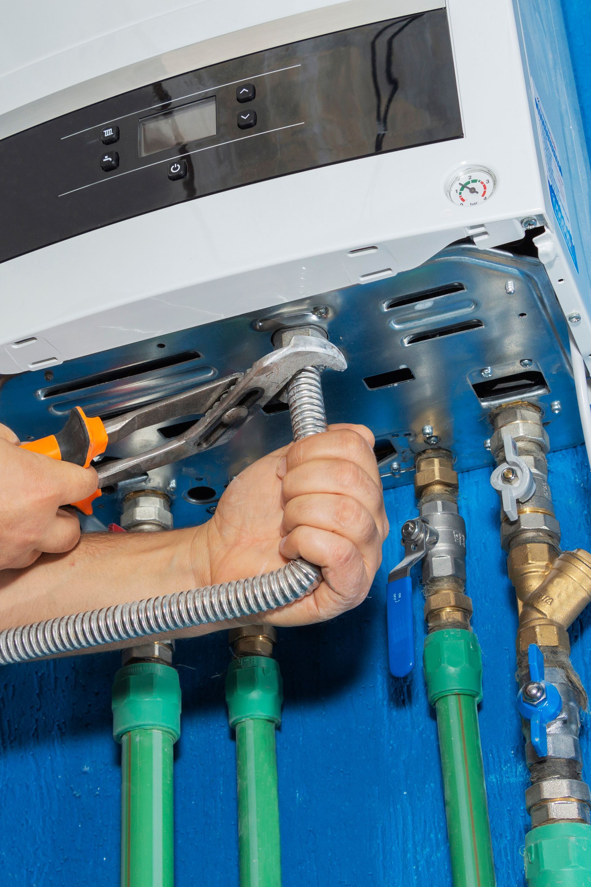 Plumber tightening a flexible gas line to a boiler with a wrench, green and brass pipes visible.
