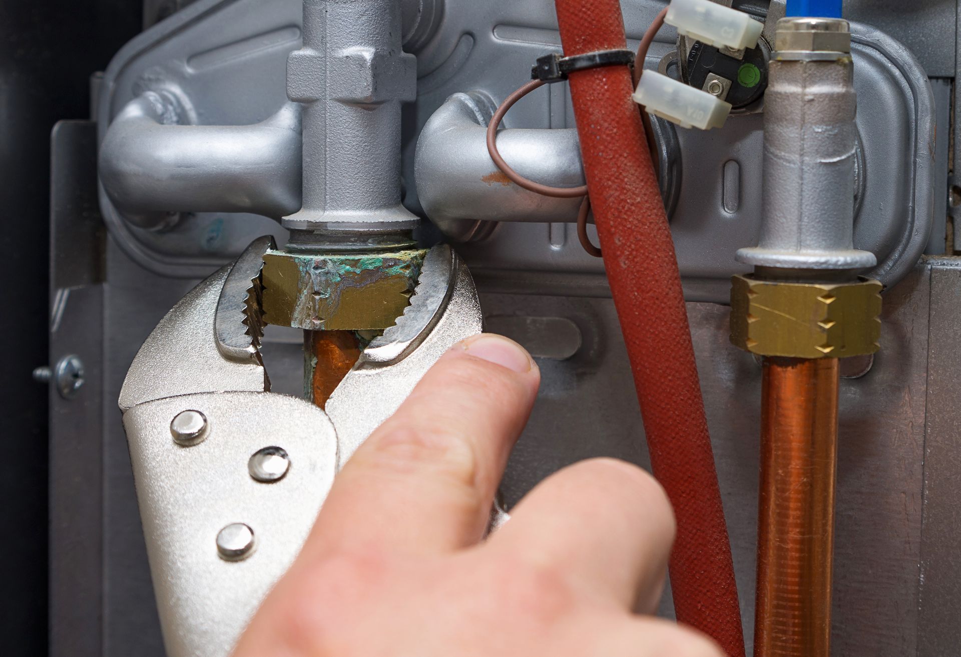 Hand using pliers to tighten a copper pipe connection on a mechanical device.