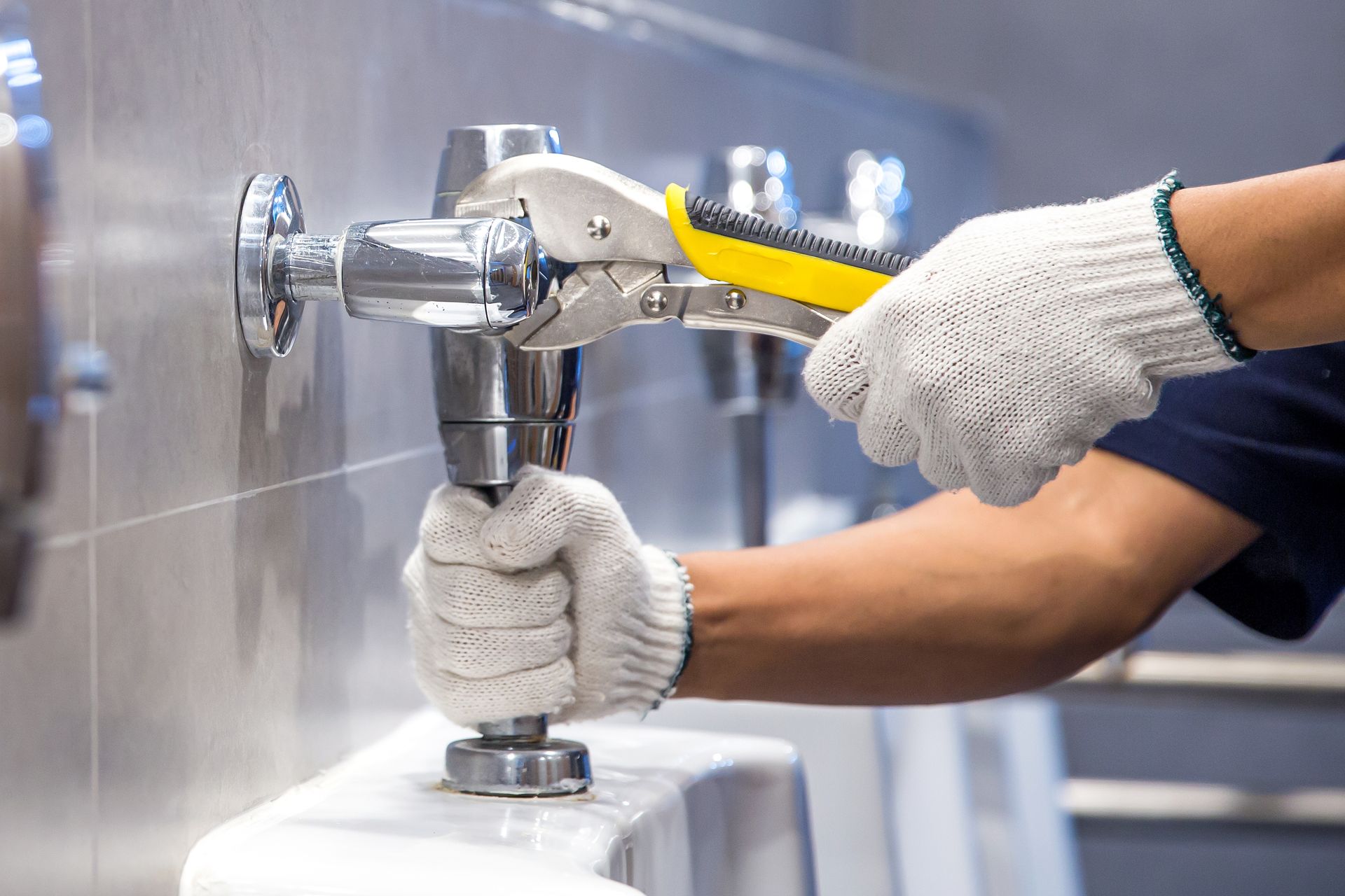 Person using adjustable pliers to tighten a component on a urinal. Wearing work gloves.