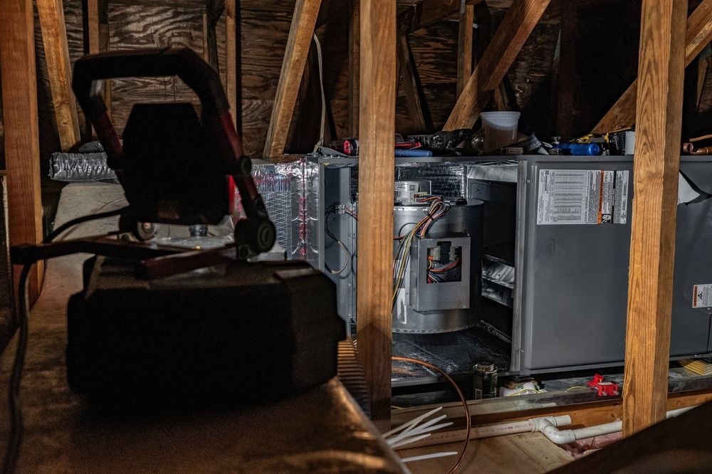 A man is working on an air conditioner in an attic.