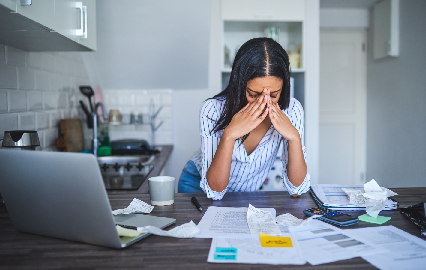 A woman is sitting at a table with papers and a laptop.