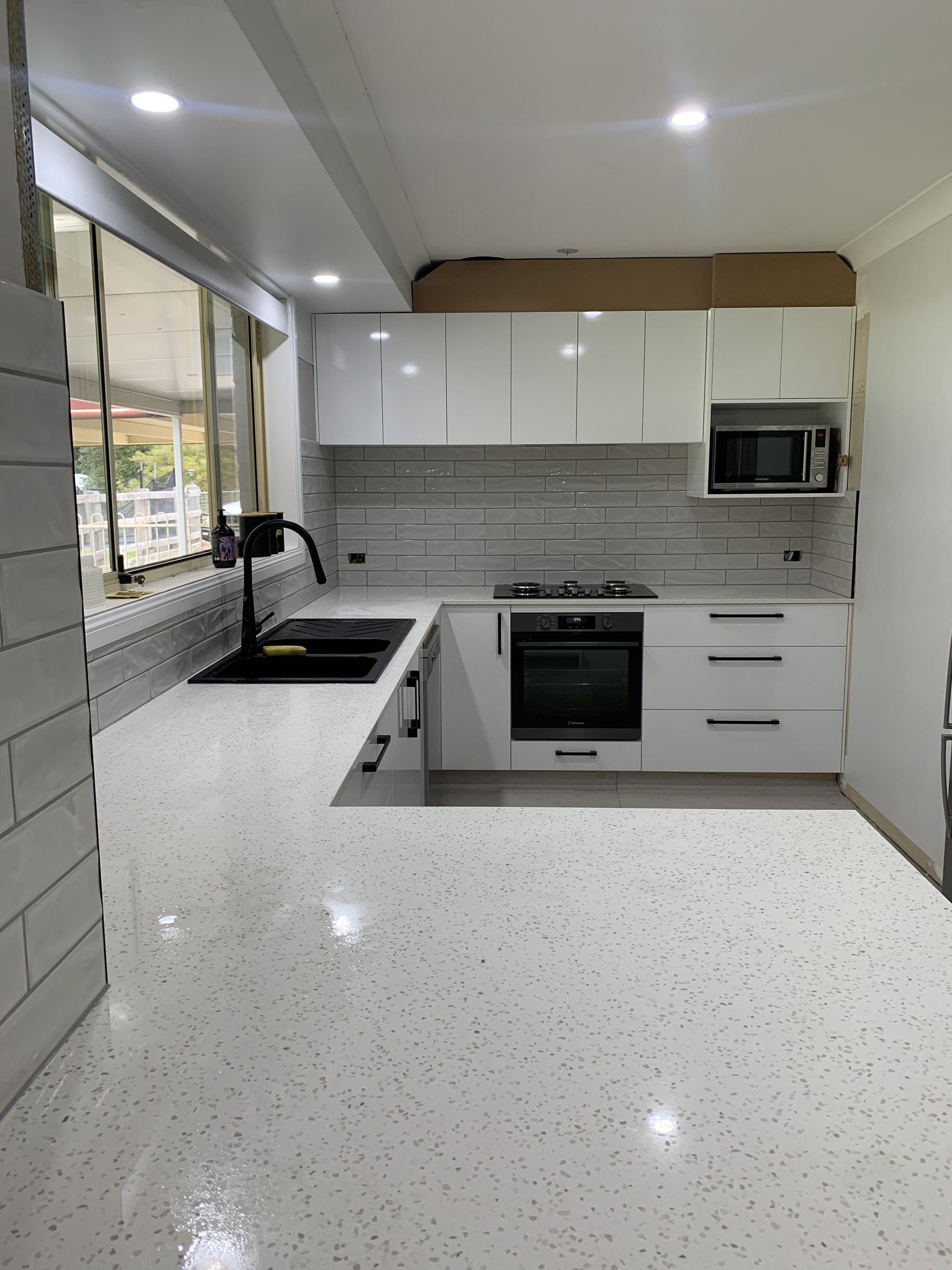 Modern bathroom featuring a glass shower with green mosaic tiles, a light wood vanity, and white floor tiles.