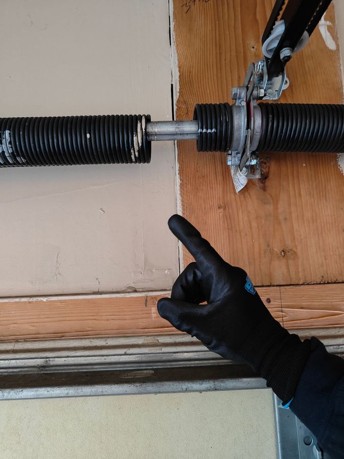 Person adjusting a metal garage door spring with a wrench and hand