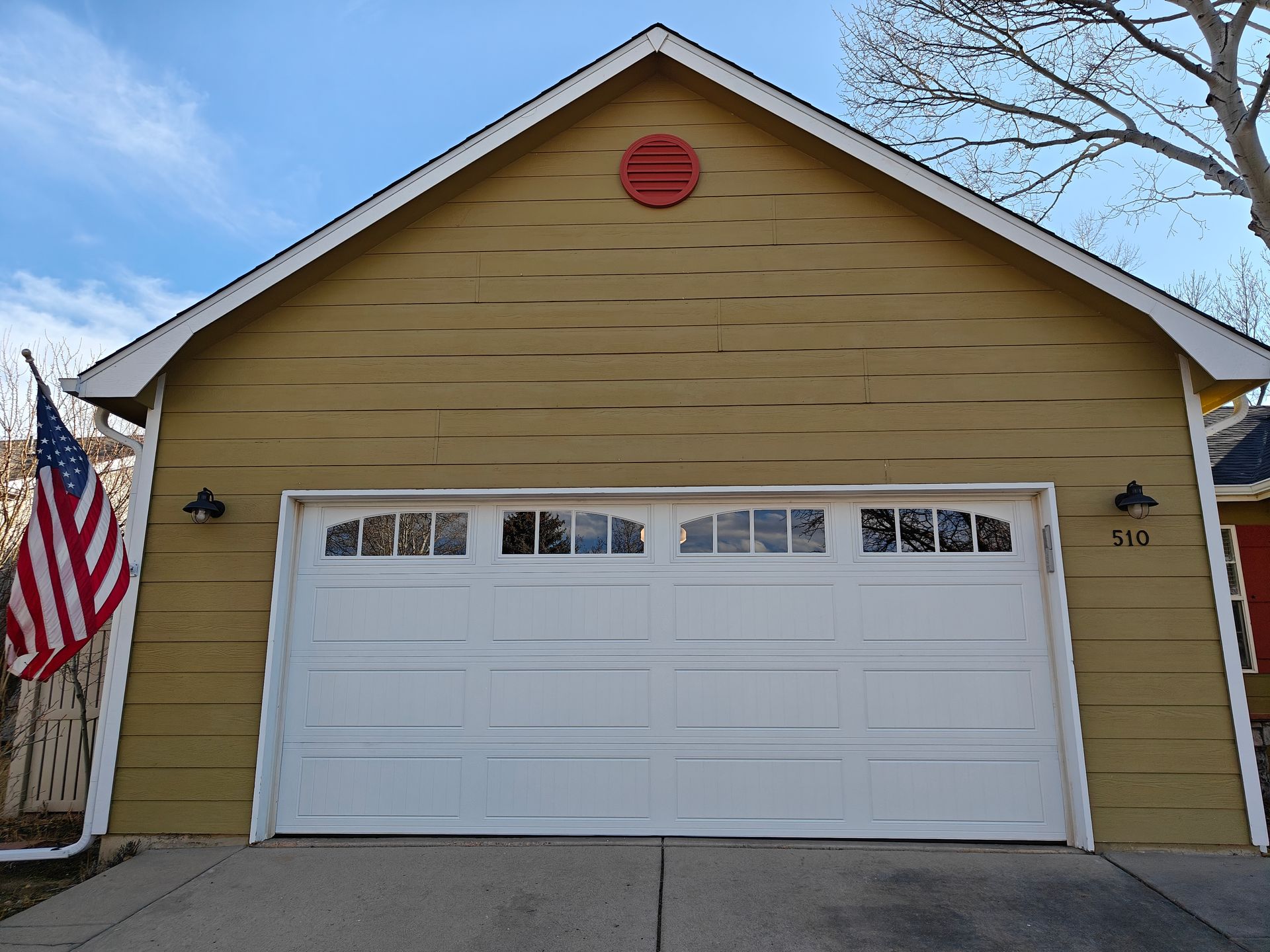 Gloved hand spraying lubricant on an overhead garage door track near a red opener unit