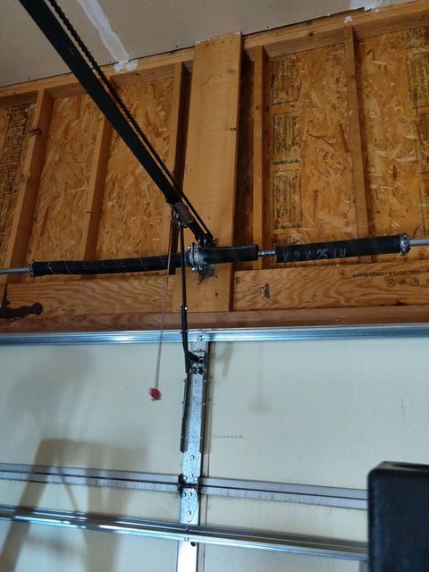 Garage door opener hardware mounted on a wooden ceiling above a garage door.