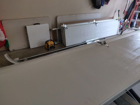 Workshop with long white boards, a yellow tool on the floor, and a curved trim piece on a workbench.