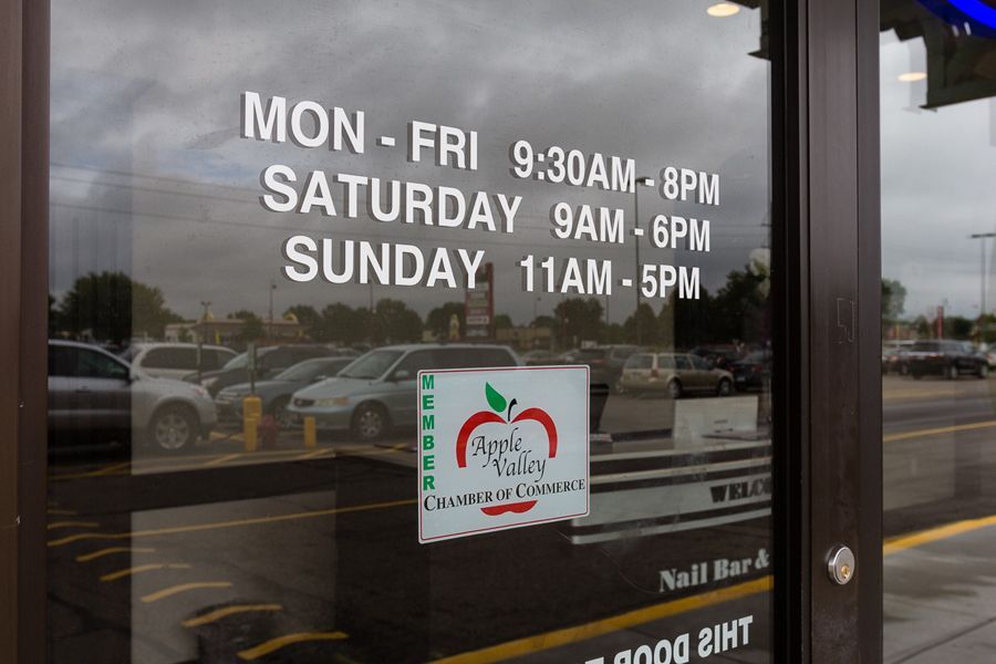 Glass door with business hours displayed, reflecting a parking lot. 