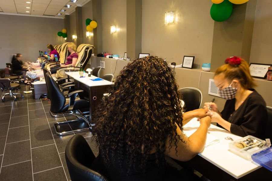 A nail salon interior with customers receiving manicures. One woman has curly hair.
