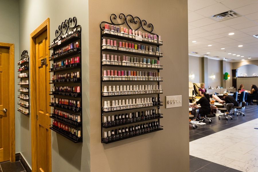 Nail salon interior with rows of nail polish on wall displays and customers receiving manicures.