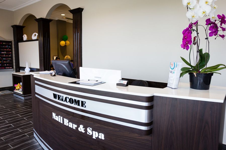 Reception desk at a nail salon. Brown and silver curved desk with welcome message and a potted orchid.