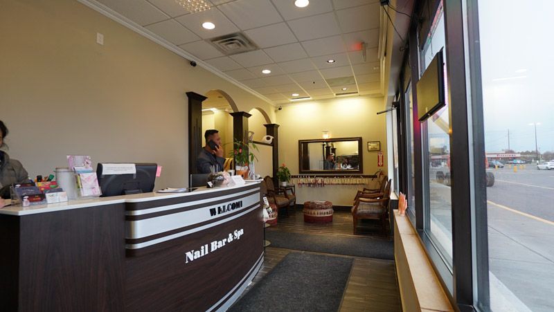 Interior view of a nail salon with a reception desk, waiting area, and large windows looking out to a street.