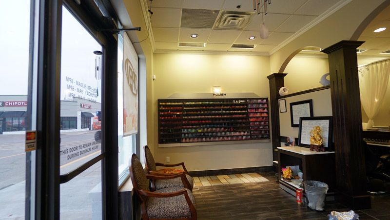 Interior of a nail salon with polish display, seating area, and view of outside shops through the windows.