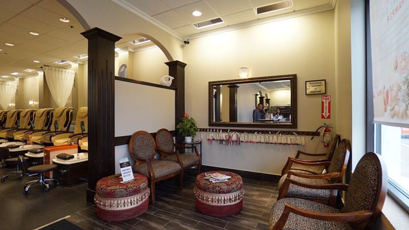 Nail salon interior with seating, manicure stations, and a mirror reflecting staff and clients.