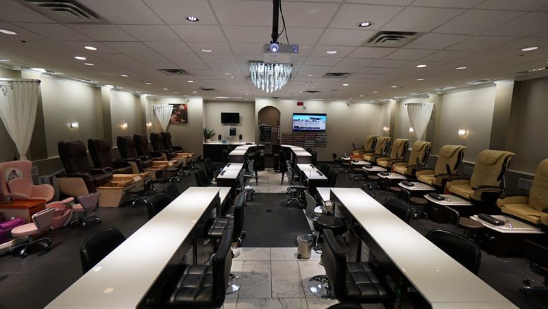 Nail salon interior with rows of manicure tables, pedicure chairs, and a chandelier.
