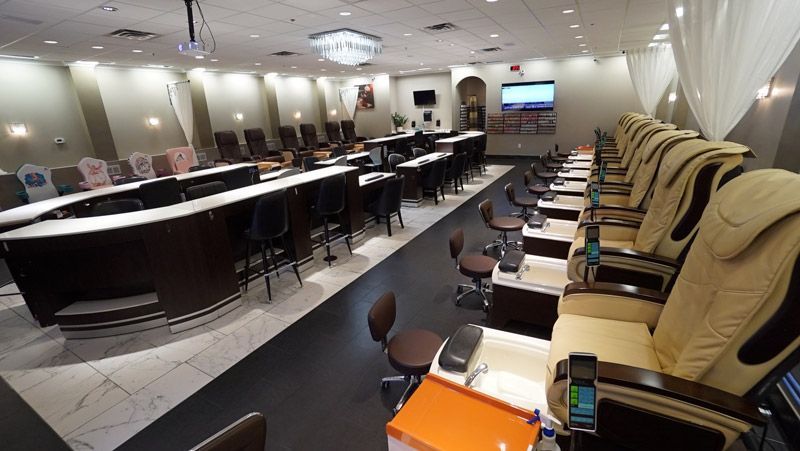 Interior of a nail salon with manicure stations and pedicure chairs. Beige and dark brown color scheme.