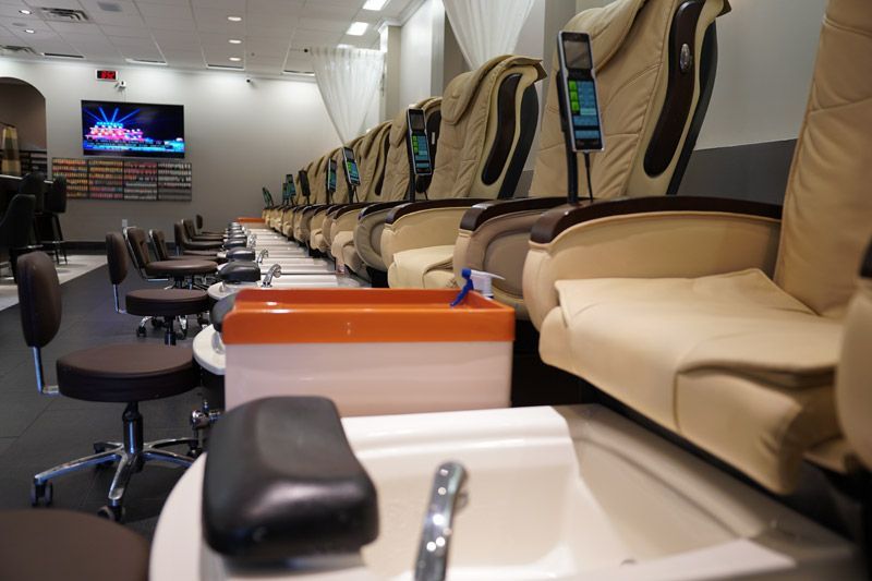 Nail salon interior with pedicure chairs and manicure stations. Beige and brown colors, clean and modern.